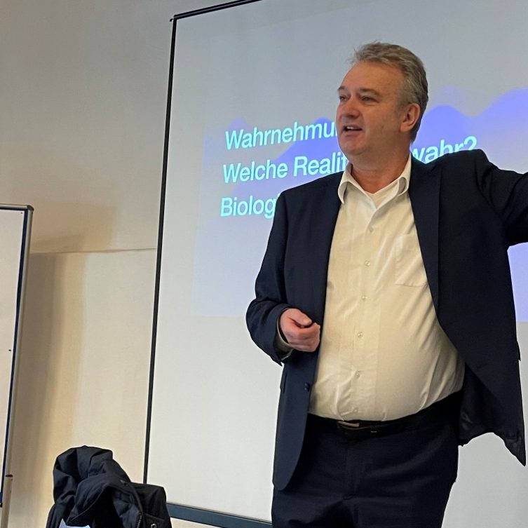 Mann in Anzug erklärt etwas vor einer Präsentationstechnik im Seminarraum.